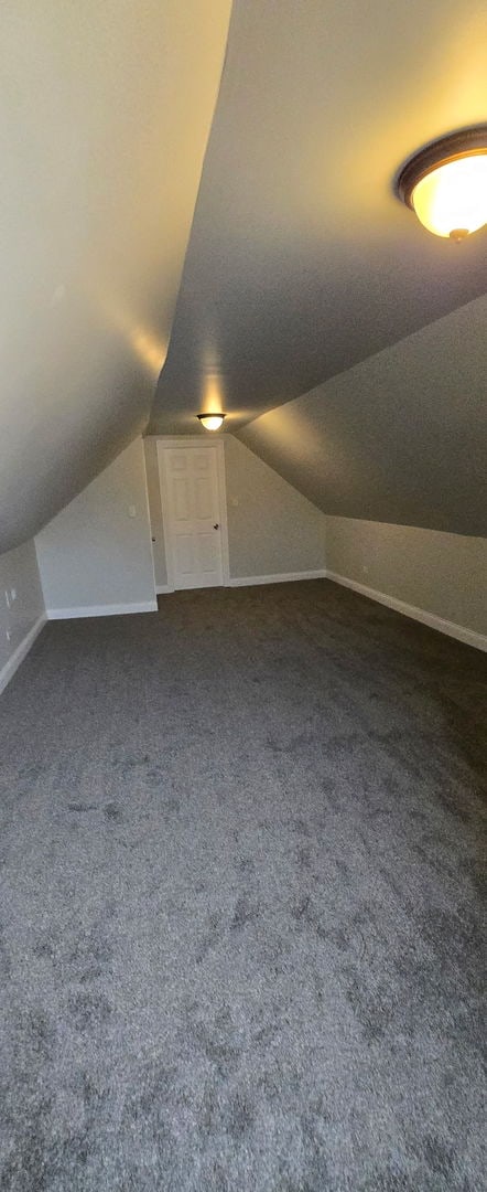 bonus room featuring vaulted ceiling, baseboards, and dark colored carpet