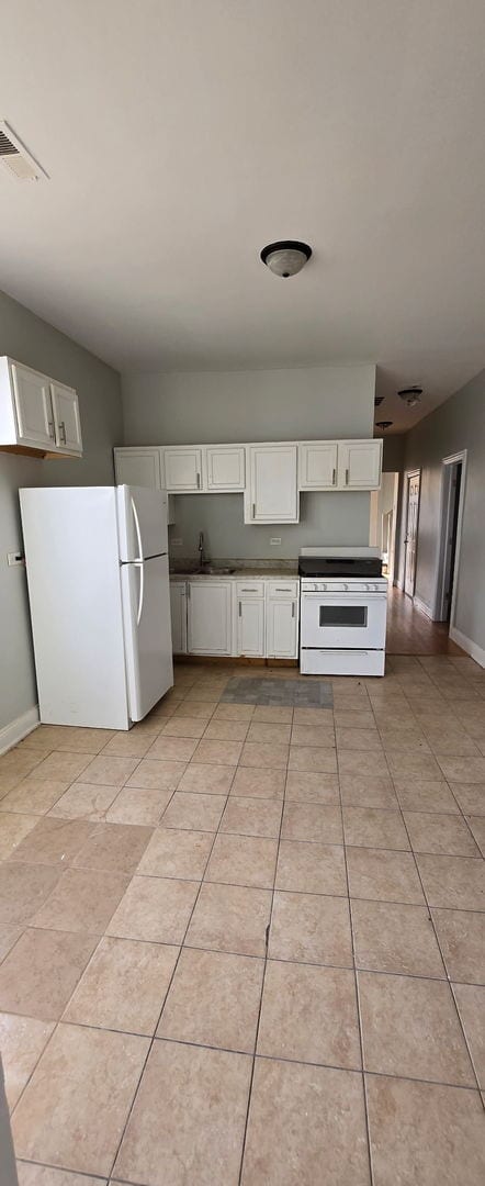 kitchen featuring light tile patterned floors, white appliances, a sink, visible vents, and white cabinets