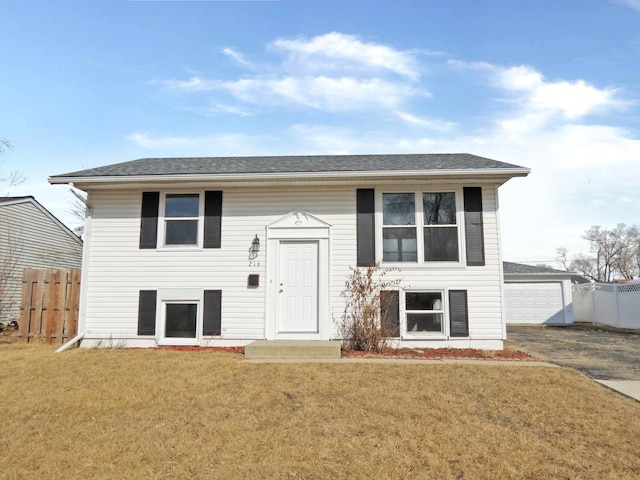 bi-level home with a front lawn, an outdoor structure, fence, and a shingled roof