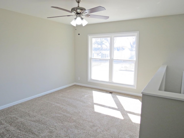 empty room with baseboards, visible vents, ceiling fan, and light colored carpet