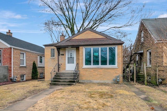 bungalow-style house with entry steps, brick siding, and a chimney