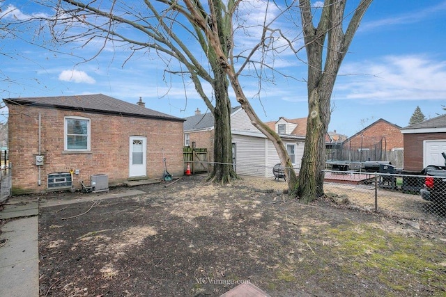 back of property featuring a trampoline, brick siding, fence, and central AC