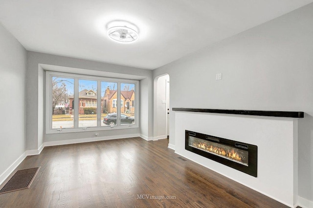 unfurnished living room featuring arched walkways, a glass covered fireplace, visible vents, and baseboards