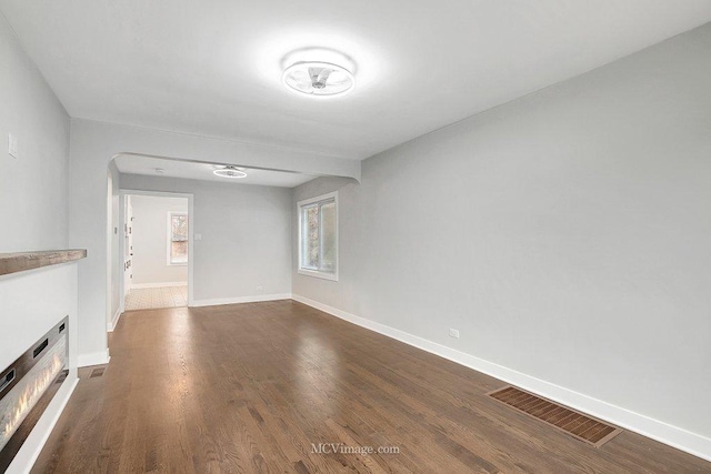 unfurnished living room with dark wood-style floors, a lit fireplace, visible vents, and baseboards