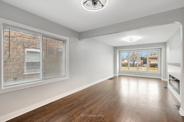 unfurnished living room with visible vents, baseboards, heating unit, dark wood-style floors, and a glass covered fireplace