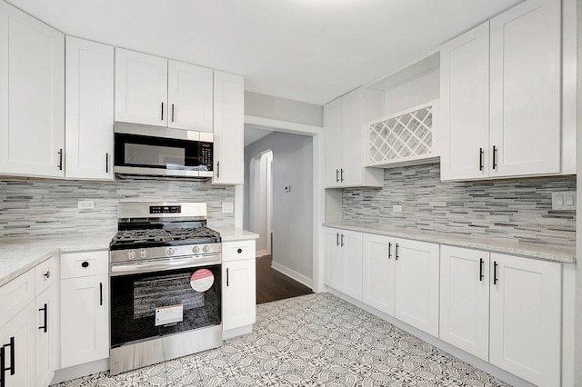 kitchen with appliances with stainless steel finishes, arched walkways, white cabinets, and tasteful backsplash