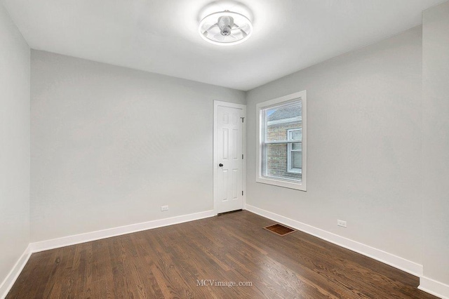 spare room with dark wood-style floors, visible vents, and baseboards