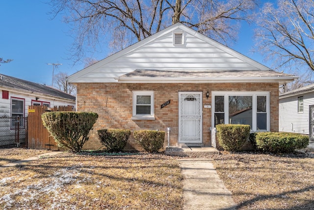 bungalow featuring brick siding, fence, and roof with shingles