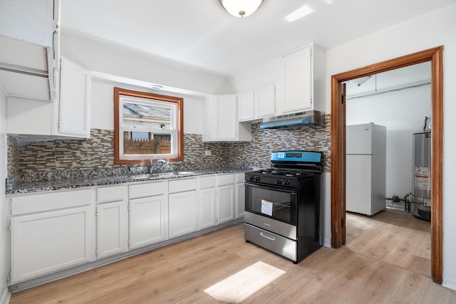 kitchen with white cabinets, freestanding refrigerator, under cabinet range hood, a sink, and gas stove