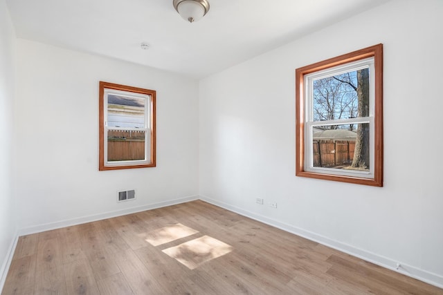 empty room with light wood-style floors, visible vents, and baseboards