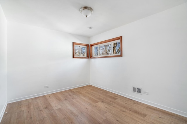 empty room with light wood-style floors, visible vents, and baseboards