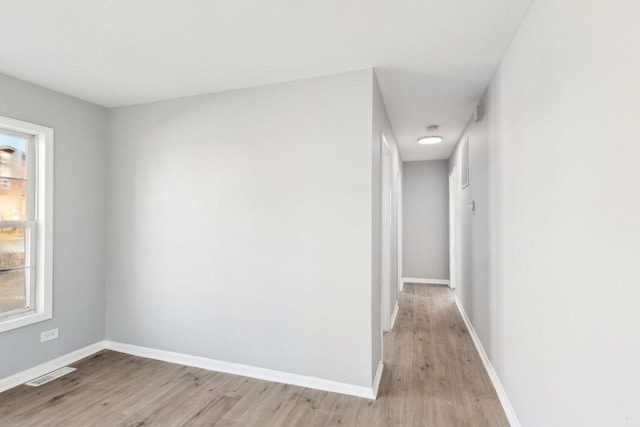 hall with light wood-type flooring, visible vents, and baseboards