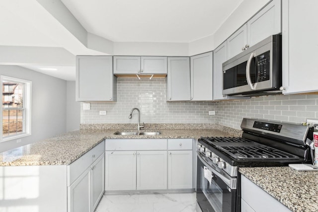 kitchen featuring marble finish floor, stainless steel appliances, a sink, light stone countertops, and a peninsula