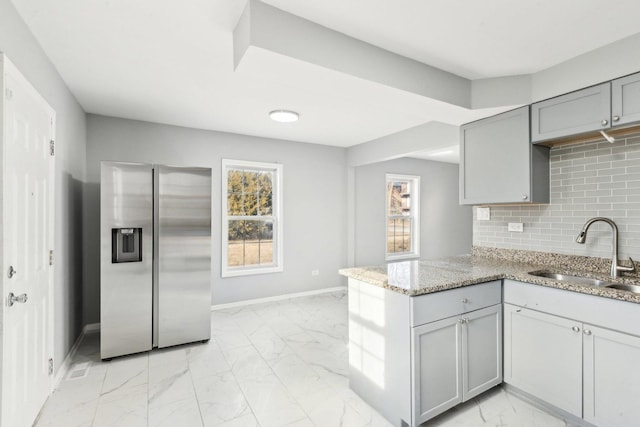 kitchen with marble finish floor, gray cabinetry, a sink, stainless steel fridge, and a peninsula