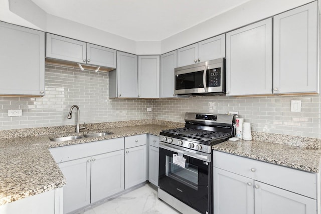 kitchen with tasteful backsplash, appliances with stainless steel finishes, light stone countertops, marble finish floor, and a sink