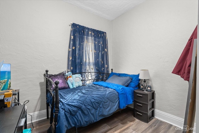 bedroom with wood finished floors, baseboards, and a textured wall