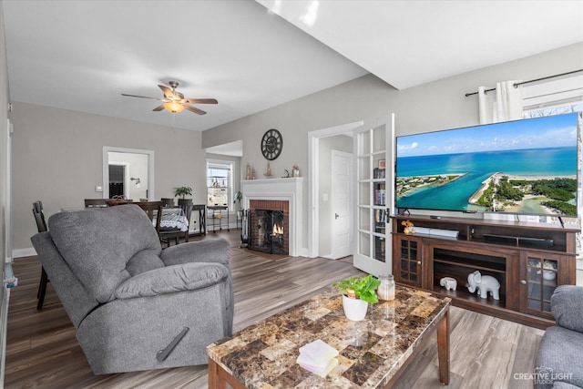 living area featuring a ceiling fan, a fireplace with flush hearth, wood finished floors, and baseboards