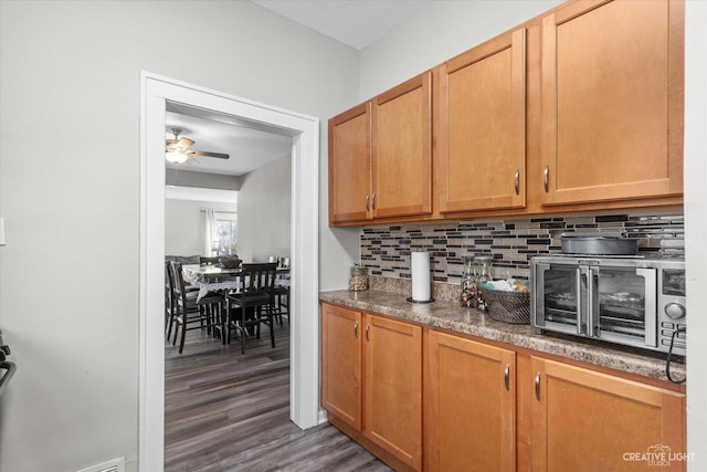 kitchen featuring ceiling fan, a toaster, decorative backsplash, brown cabinets, and dark wood-style flooring