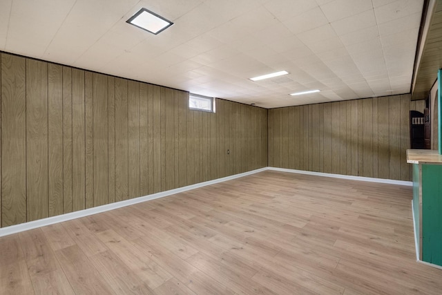 basement featuring baseboards, wood walls, and light wood finished floors