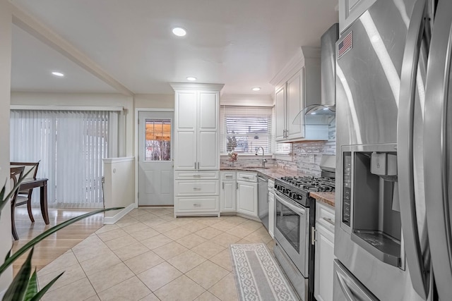 kitchen with stainless steel appliances, wall chimney range hood, a sink, and white cabinets