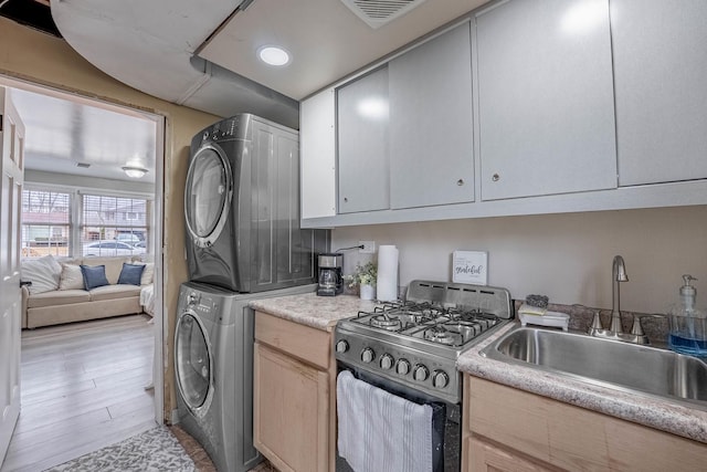 kitchen featuring stainless steel range with gas cooktop, stacked washer / drying machine, light countertops, visible vents, and a sink