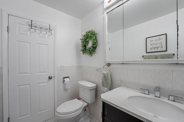 half bathroom featuring tile walls, a wainscoted wall, vanity, and toilet