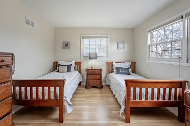 bedroom featuring baseboards, visible vents, multiple windows, and wood finished floors