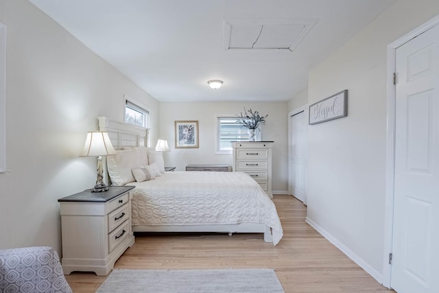 bedroom with light wood-style floors, attic access, and baseboards