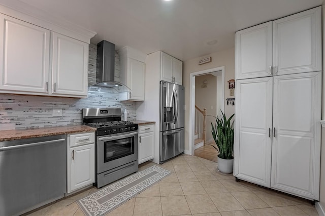 kitchen featuring appliances with stainless steel finishes, white cabinetry, wall chimney range hood, and tasteful backsplash