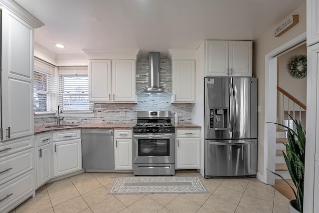 kitchen featuring light tile patterned floors, stainless steel appliances, a sink, white cabinetry, and wall chimney exhaust hood