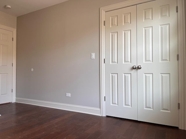 unfurnished bedroom featuring a closet, baseboards, and dark wood-style flooring