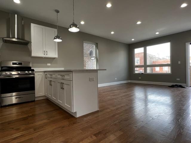 kitchen featuring a peninsula, stainless steel gas range oven, wall chimney range hood, and white cabinets