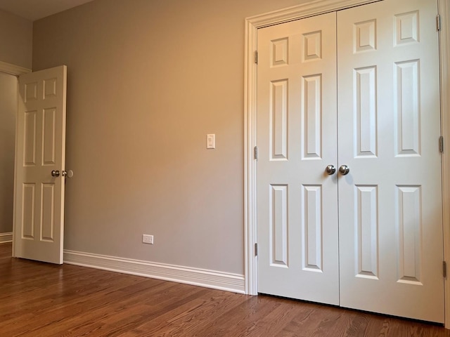 unfurnished bedroom with dark wood-style flooring, a closet, and baseboards