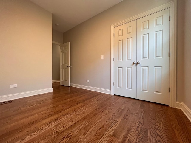 unfurnished bedroom with a closet, dark wood-style flooring, visible vents, and baseboards