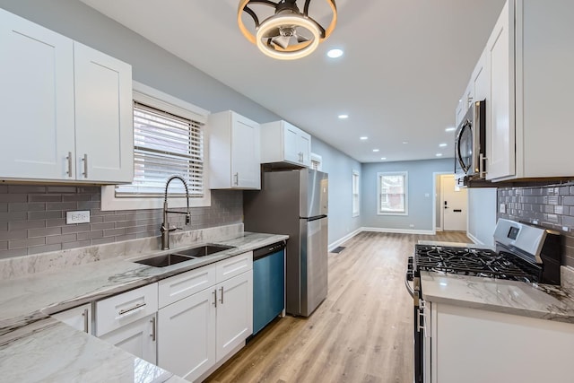 kitchen with light wood-style flooring, appliances with stainless steel finishes, white cabinets, a sink, and light stone countertops