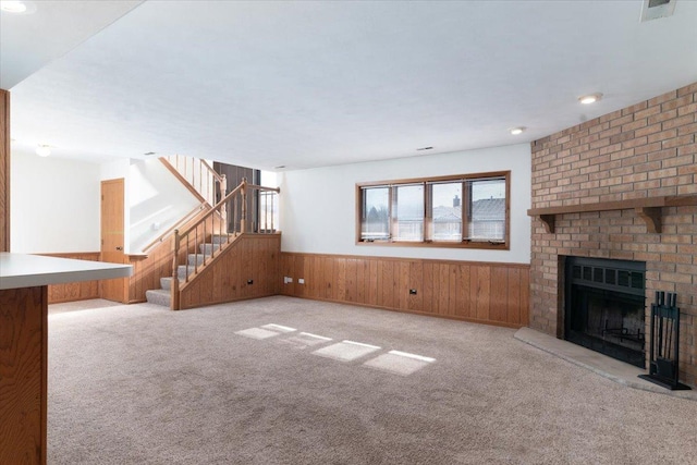 unfurnished living room with stairway, wainscoting, carpet flooring, and a brick fireplace