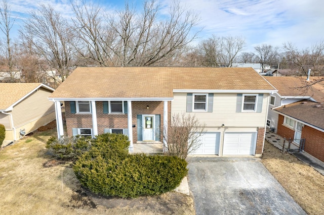 bi-level home with an attached garage, a shingled roof, aphalt driveway, and brick siding