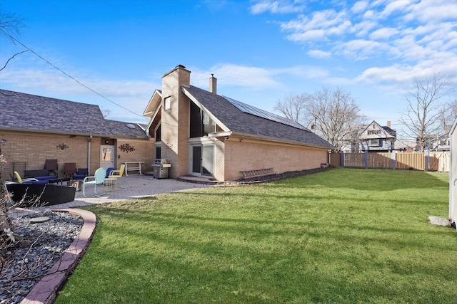 back of property with roof mounted solar panels, a yard, brick siding, fence private yard, and a patio area