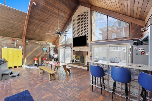 interior space with high vaulted ceiling, wooden ceiling, a fireplace, wood walls, and brick floor