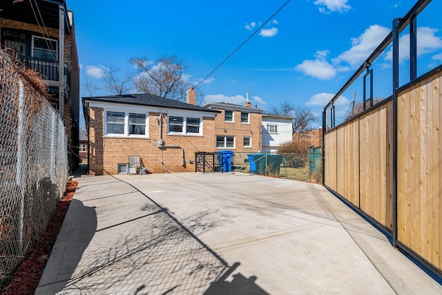 rear view of house with brick siding, a patio area, a chimney, and fence