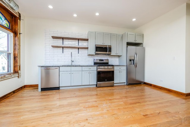 kitchen featuring light wood-style flooring, open shelves, a sink, backsplash, and appliances with stainless steel finishes