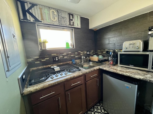 kitchen with a sink, backsplash, dark brown cabinetry, appliances with stainless steel finishes, and light countertops