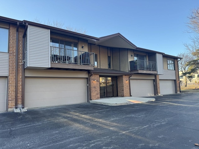 multi unit property with board and batten siding, an attached garage, brick siding, and driveway