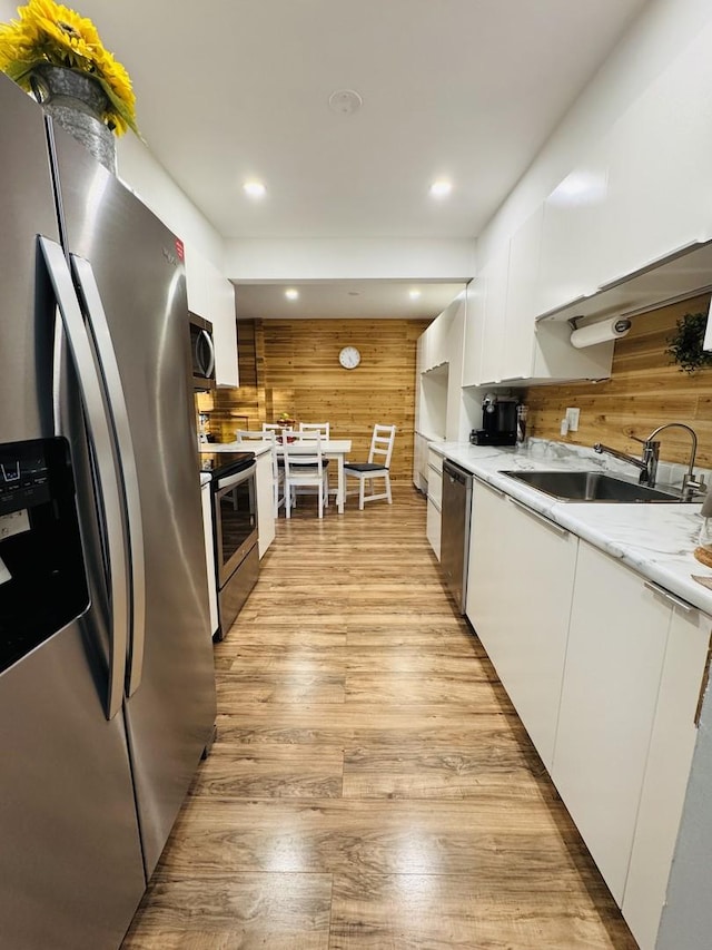 kitchen featuring wood walls, light wood-type flooring, appliances with stainless steel finishes, white cabinetry, and a sink