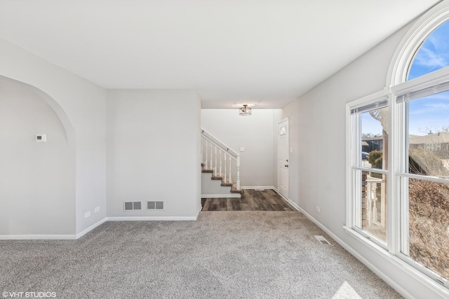 carpeted spare room with visible vents, stairway, and baseboards