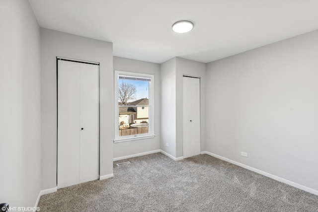 unfurnished bedroom with baseboards, carpet flooring, visible vents, and multiple closets