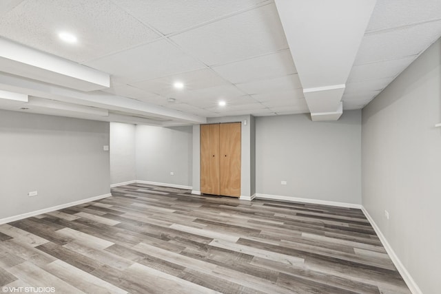 finished basement featuring recessed lighting, wood finished floors, a paneled ceiling, and baseboards