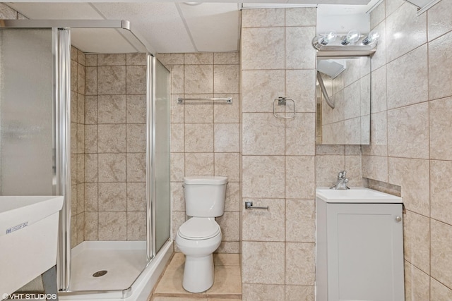 bathroom featuring tile walls, toilet, a stall shower, vanity, and tile patterned floors