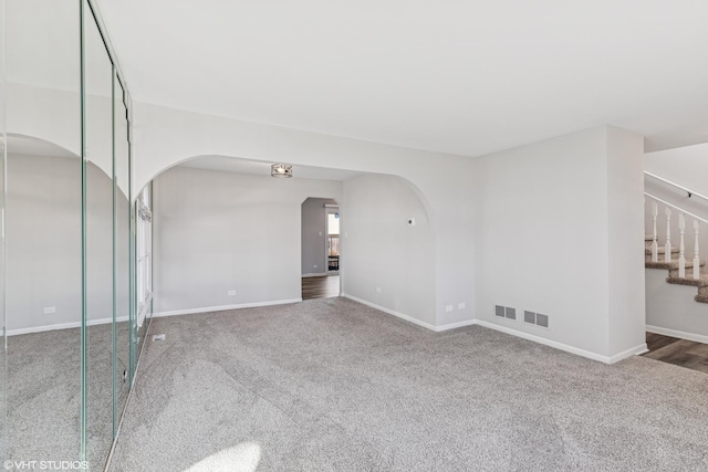 carpeted spare room featuring visible vents, stairs, arched walkways, and baseboards