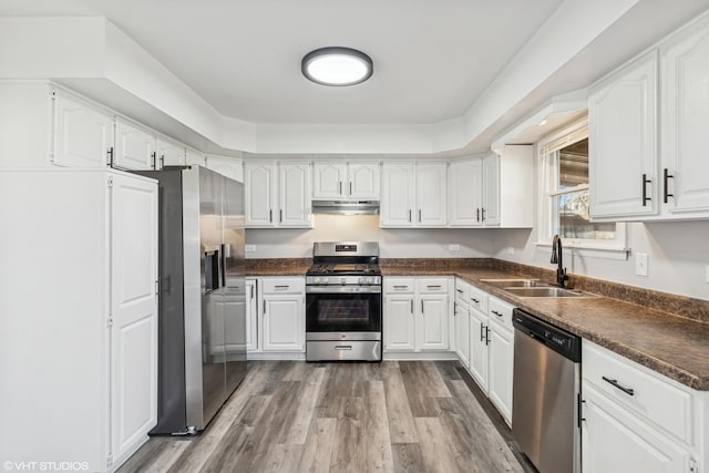 kitchen featuring dark countertops, stainless steel appliances, under cabinet range hood, white cabinetry, and a sink